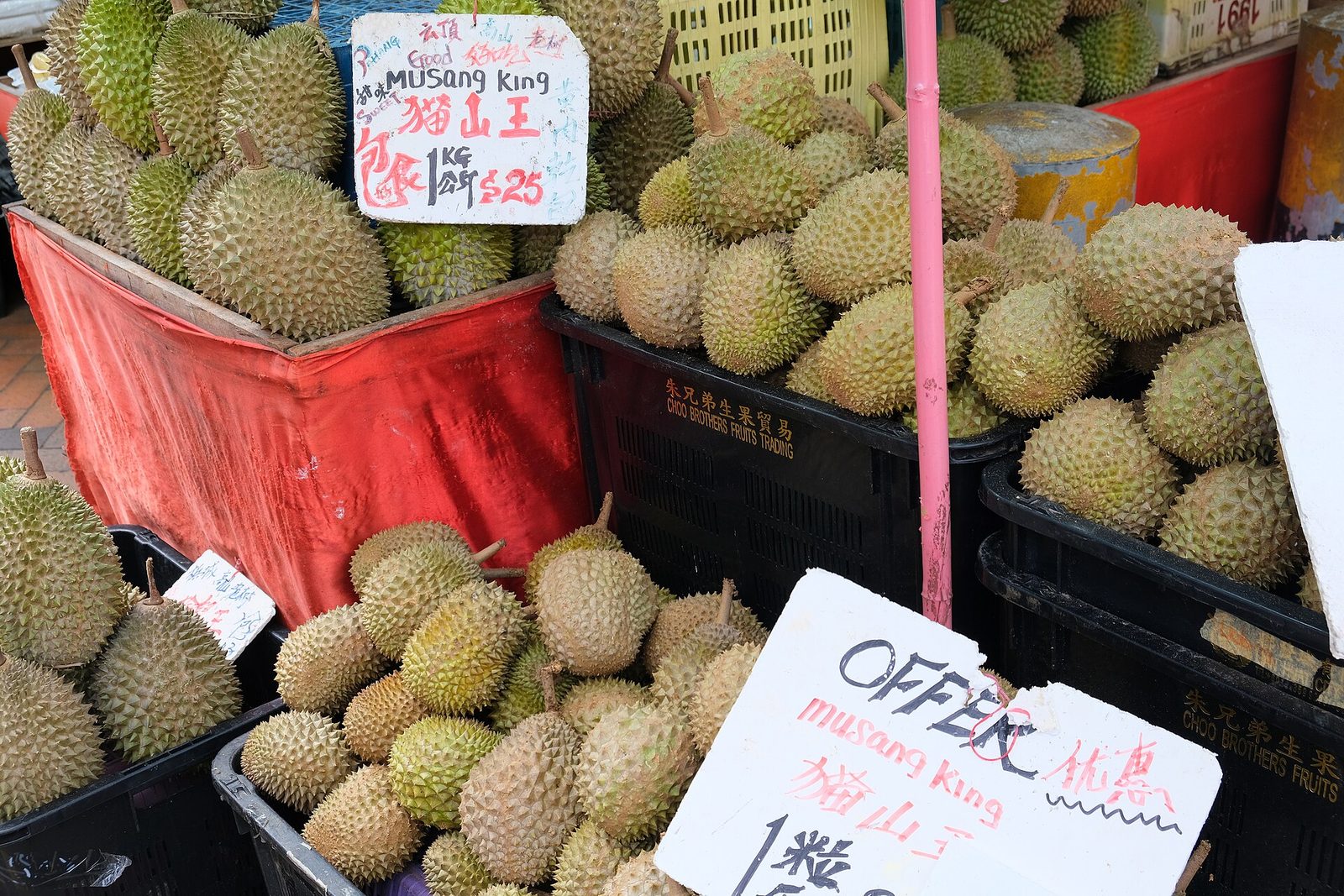Étal de durians empilés dans des caisses rouges, avec des pancartes de prix manuscrites, dans le quartier de Chinatown