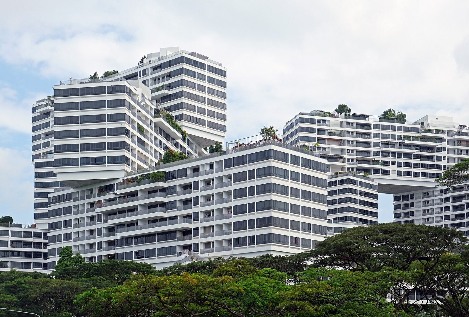 Les immeubles empilés en quinconce de la résidence The Interlace, entourés de végétation, sous un ciel nuageux