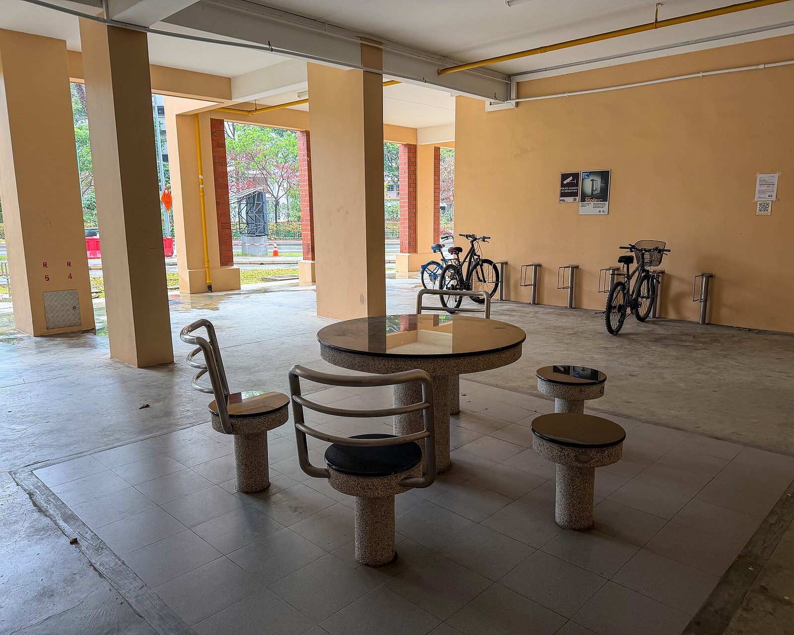 Le rez-de-chaussée ouvert d'un immeuble HDB à Tampines, avec une table et des tabourets en pierre et des vélos garés