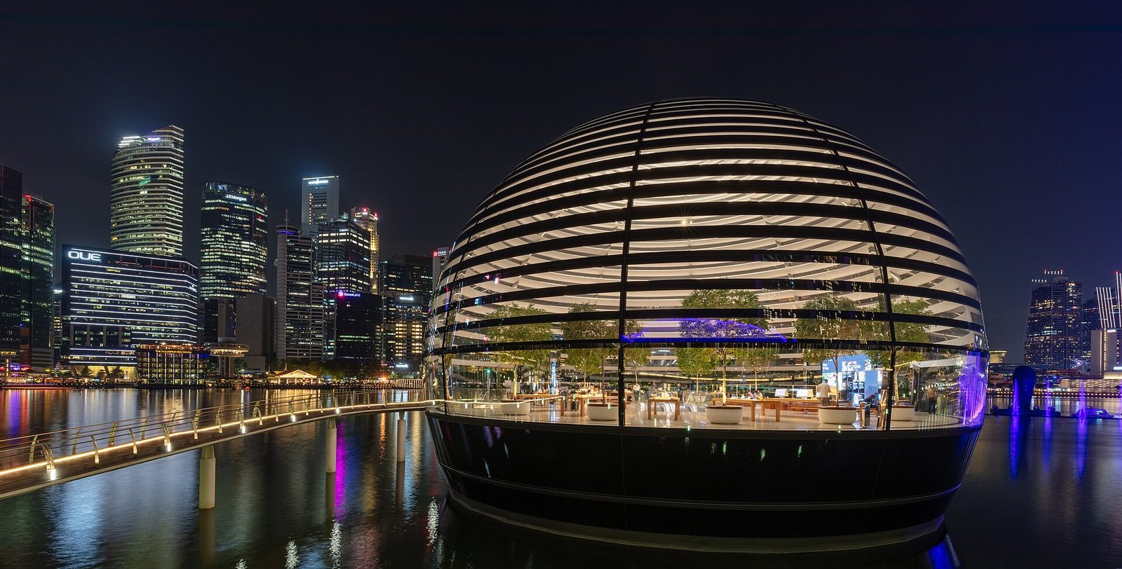 La sphère de verre illuminée de l'Apple Store de Marina Bay Sands posée sur l'eau, la nuit, devant les gratte-ciel du quartier d'affaires