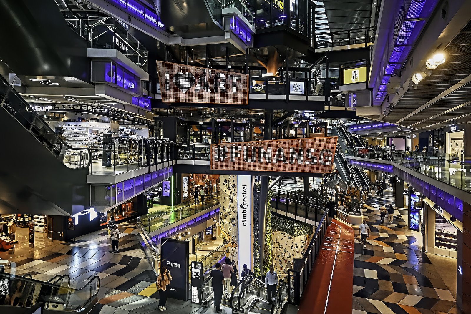 L'intérieur de Funan sur plusieurs niveaux, avec les panneaux #FUNANSG et I love ART, le mur d'escalade à droite et la piste cyclable rouge au sol