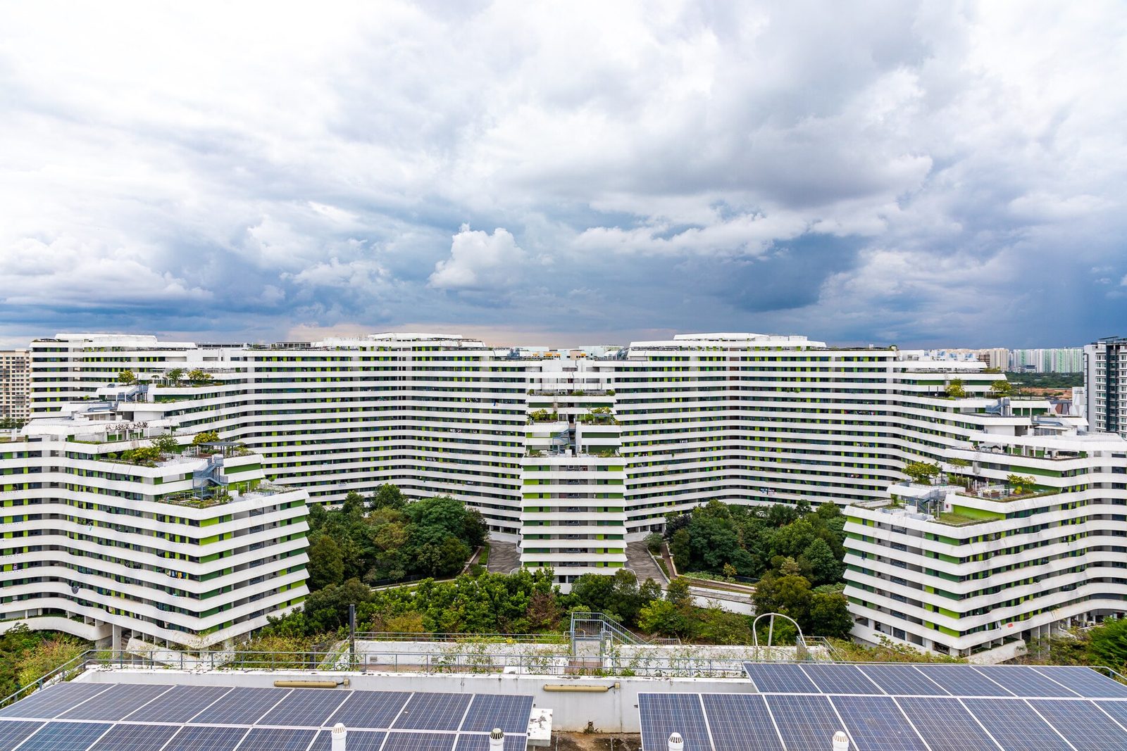 Vue en hauteur des immeubles blancs en gradins de Waterway Terrace I, avec des toits végétalisés et une cour arborée, sous un ciel nuageux