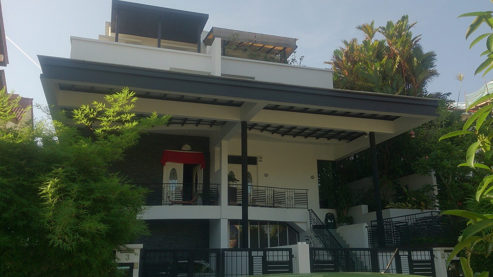 Façade blanche et grise d'une maison jumelée moderne à plusieurs niveaux, avec un grand auvent et un jardin planté de bambous