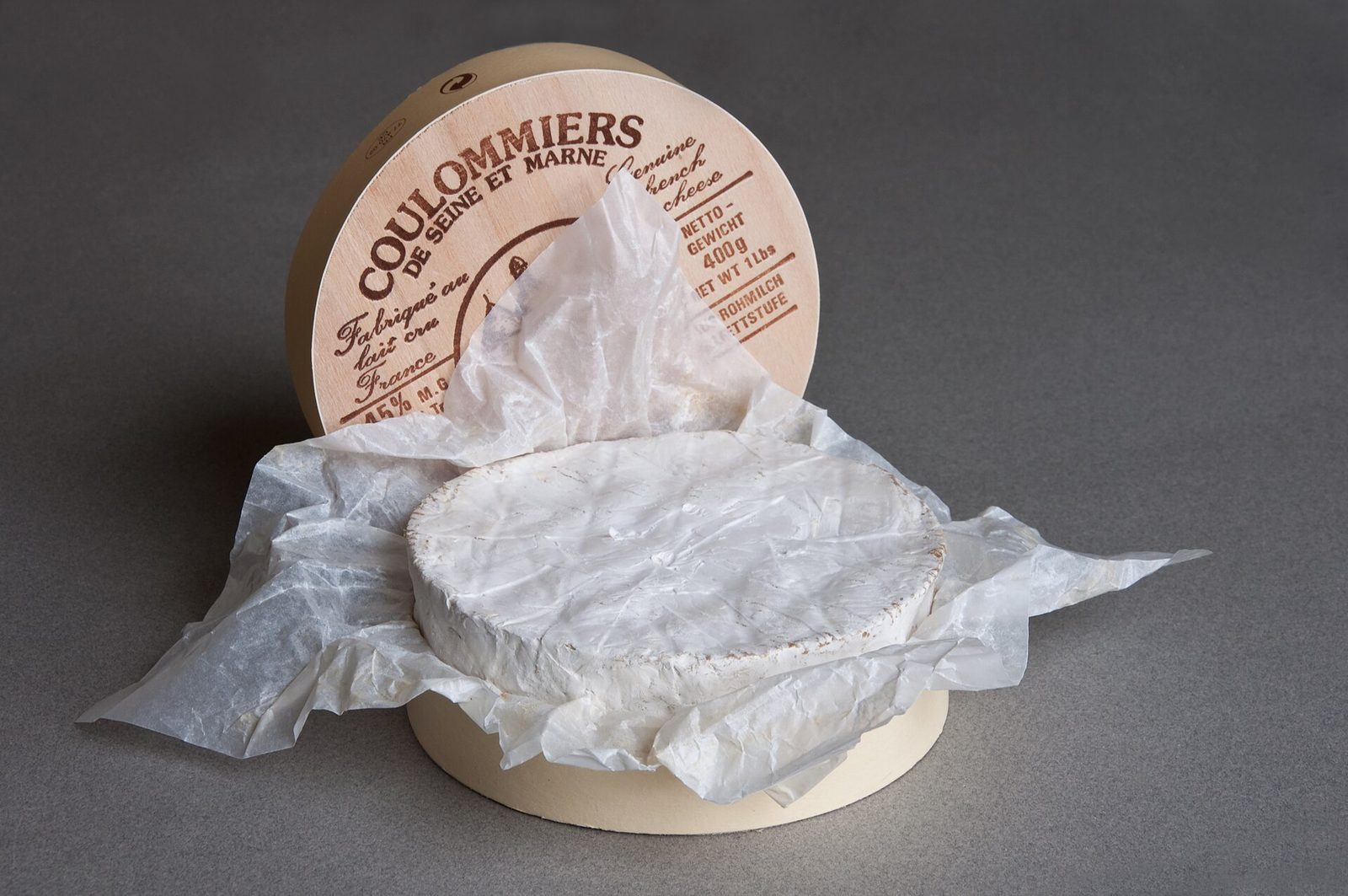 Un coulommiers entier à croûte blanche posé sur son papier, devant sa boîte ronde étiquetée