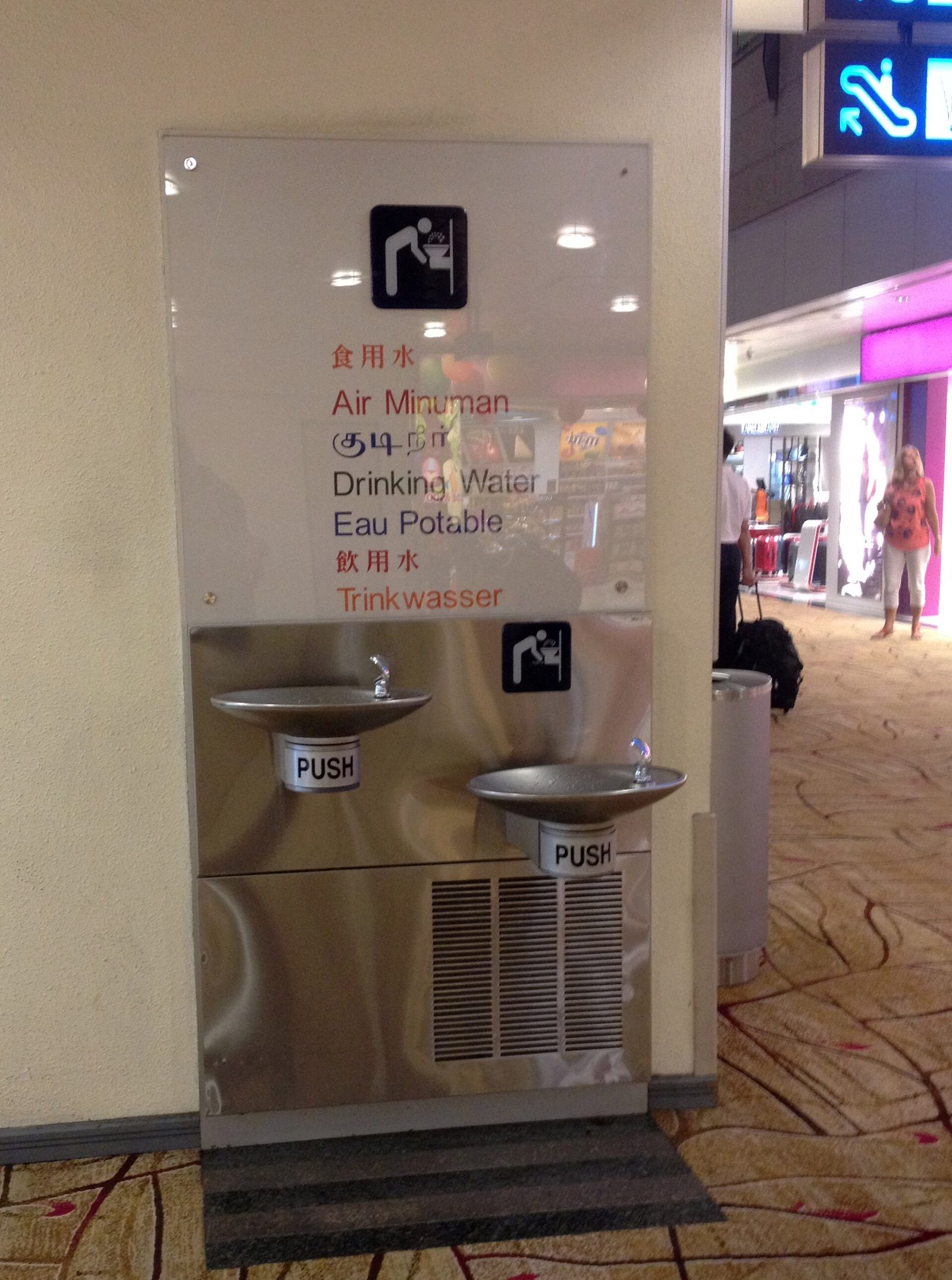 Fontaine à eau de l'aéroport de Changi surmontée d'un panneau Eau potable en chinois, malais, tamoul, anglais, français et allemand