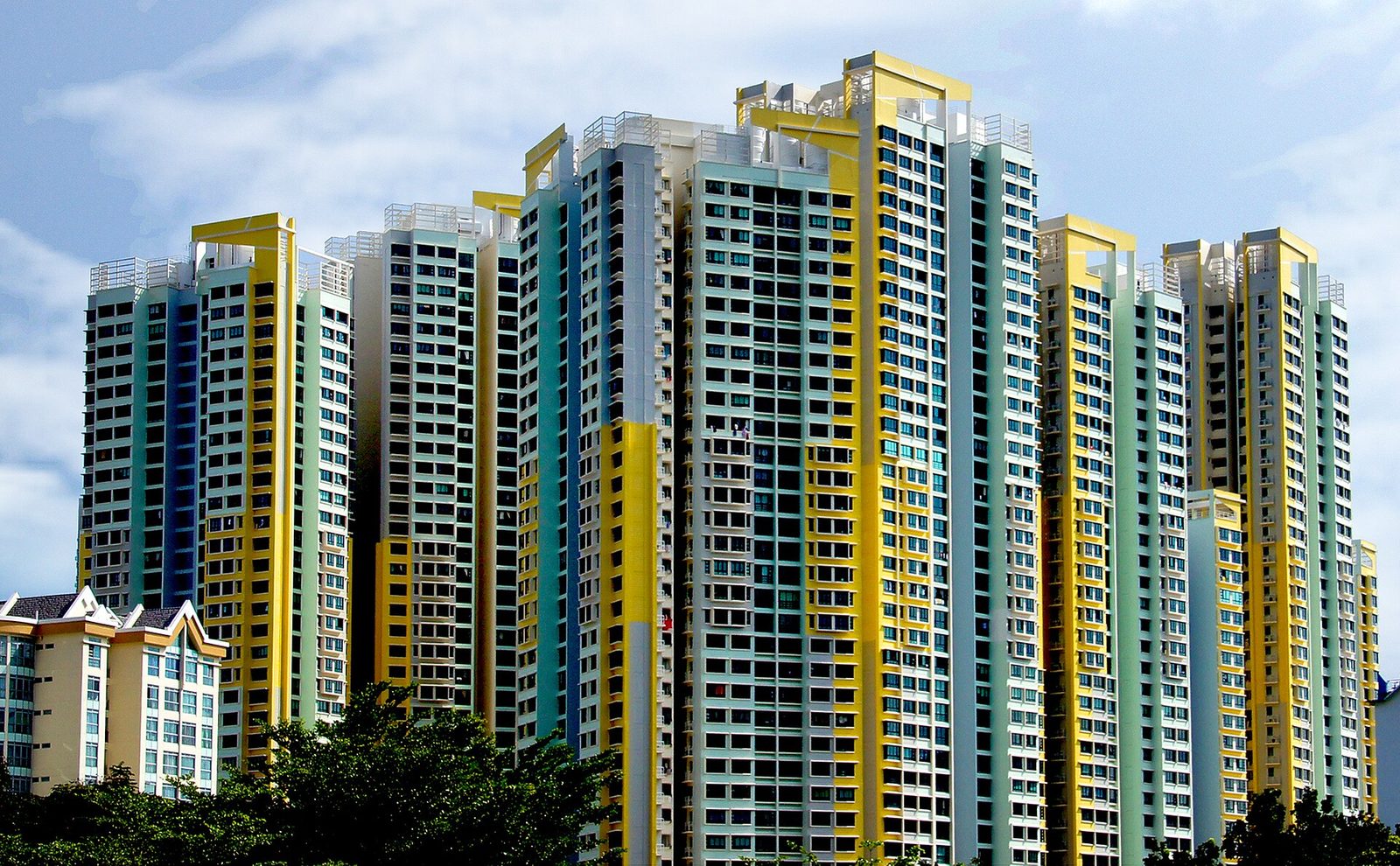 Tours de logements publics HDB aux façades jaunes, vertes et blanches, sous un ciel bleu