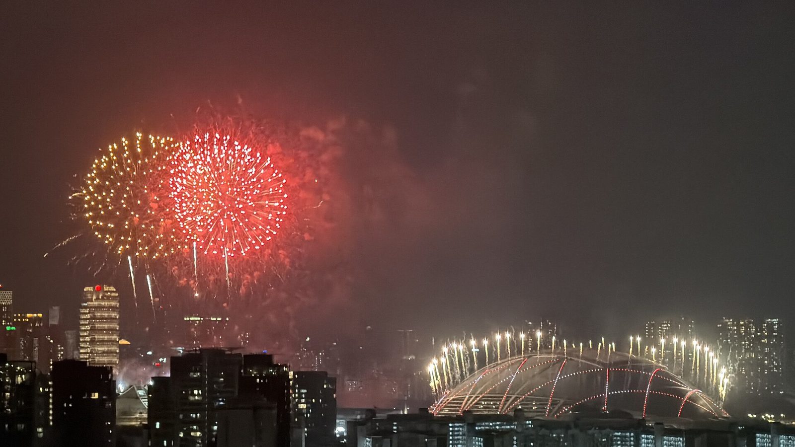 Feux d'artifice rouges et dorés au-dessus du toit en dôme du National Stadium, illuminé de fusées, au milieu des tours d'habitation