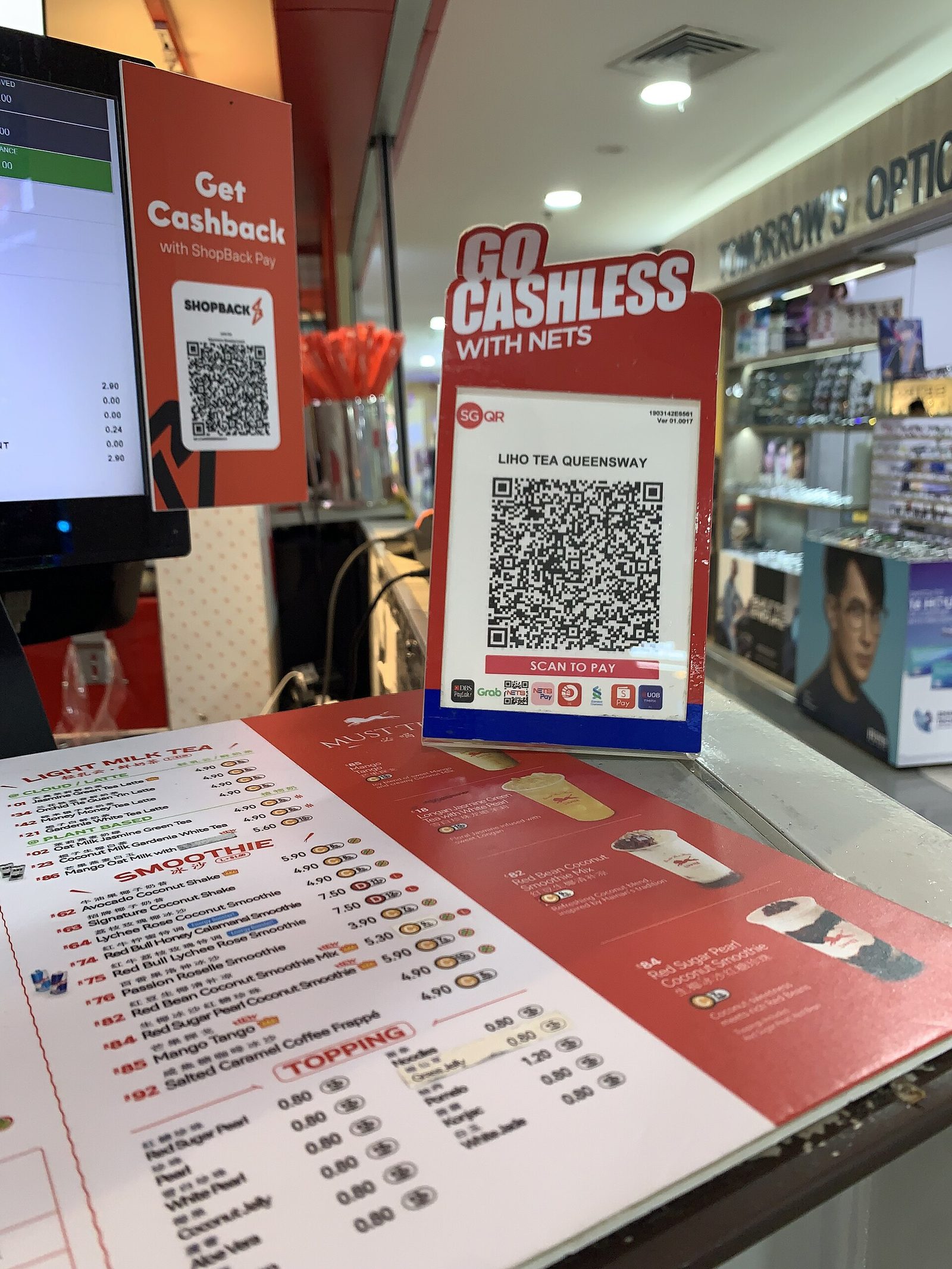 Un présentoir SGQR « Scan to pay » posé sur le comptoir d'un salon de thé, avec les logos des applications acceptées en bas du code
