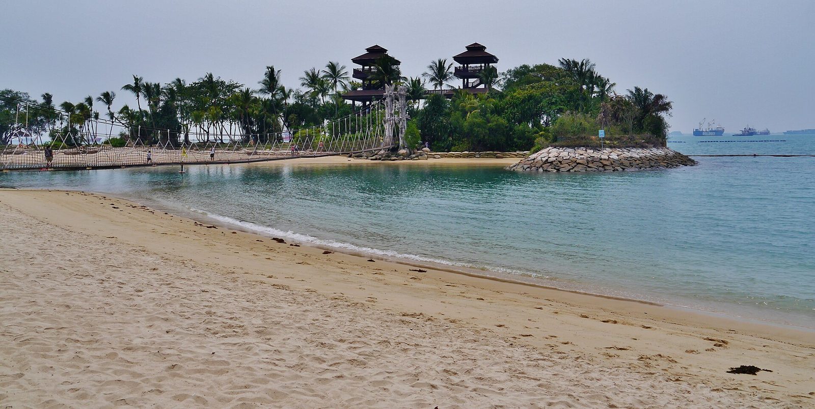 La plage de Palawan à Sentosa, avec le pont de corde suspendu qui mène à l'îlot boisé surmonté de deux tours d'observation