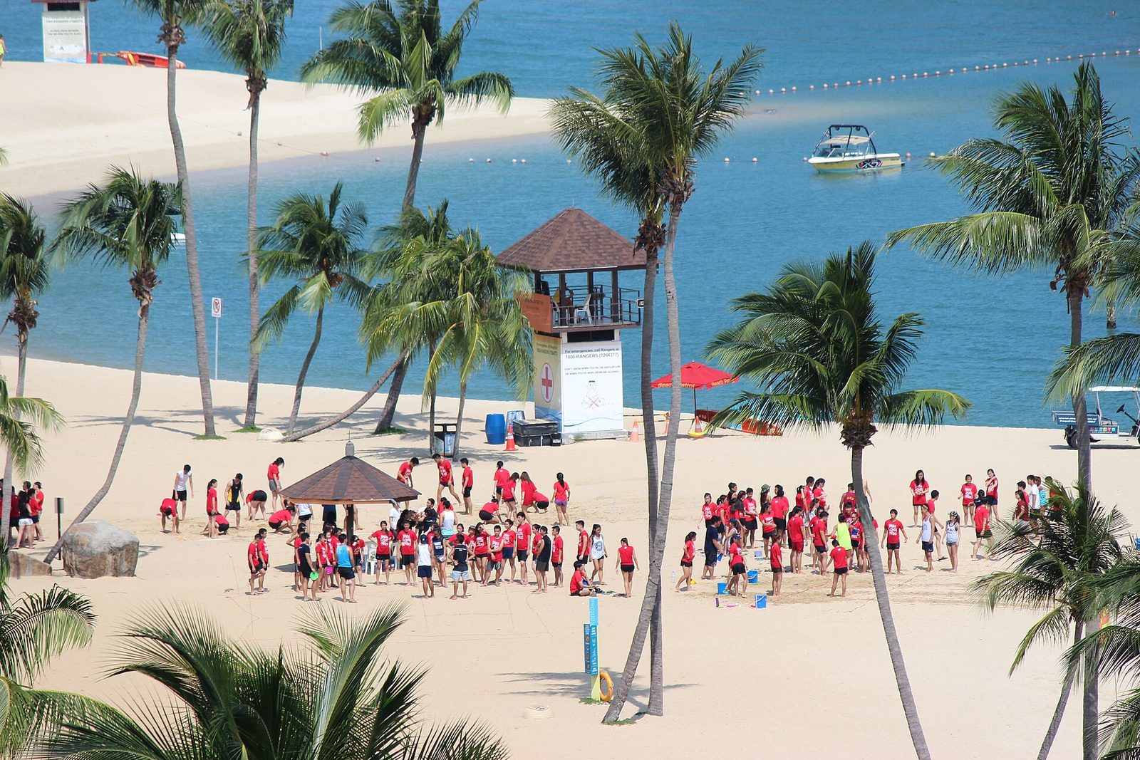 Poste de sauveteurs sur la plage de Siloso à Sentosa, entre les cocotiers, avec le lagon bleu délimité par une ligne de bouées