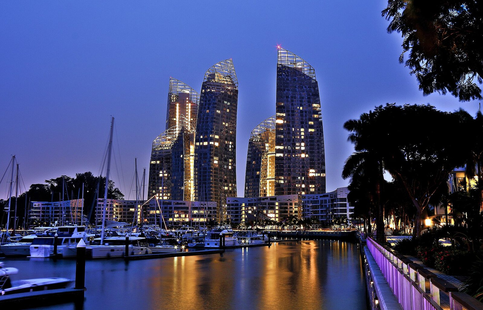 Les tours ondulées de Reflections at Keppel Bay illuminées à la tombée de la nuit, au-dessus d'une marina où sont amarrés des voiliers