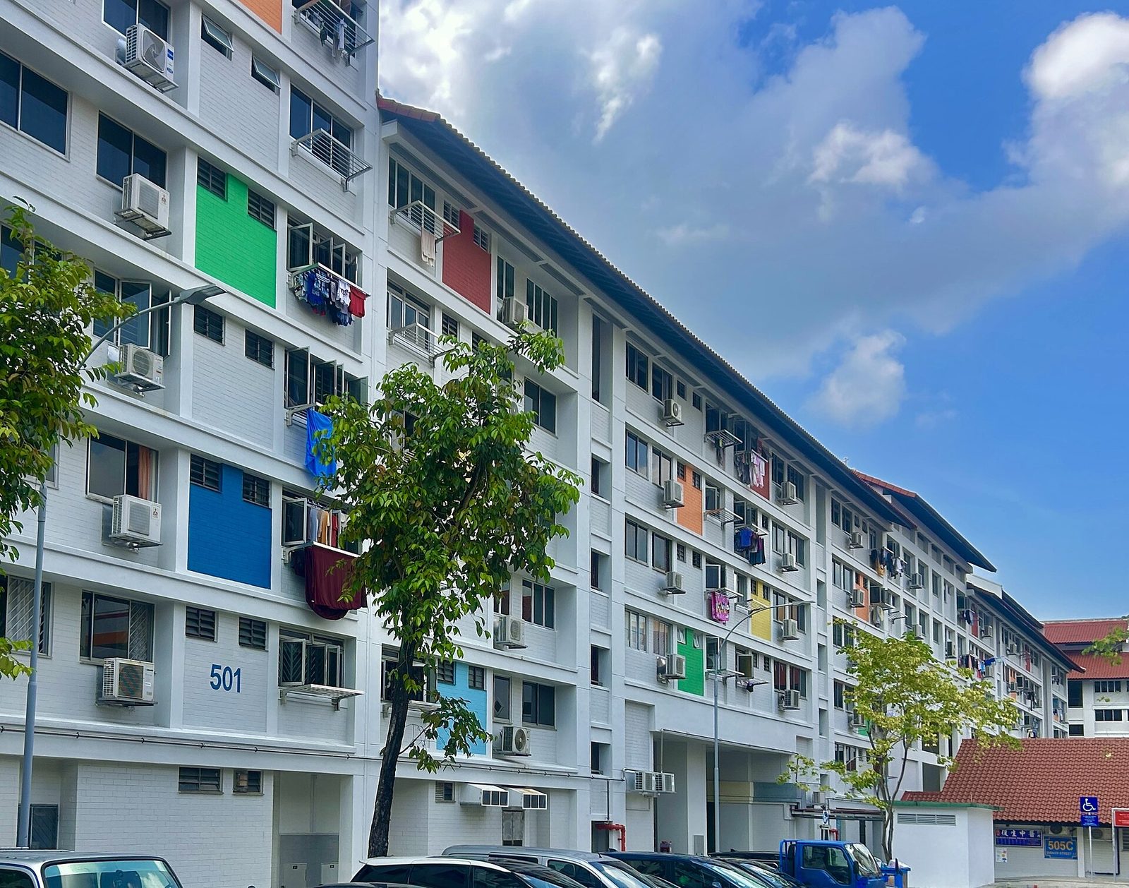 Façade blanche d'un immeuble HDB à Bishan, avec des panneaux de couleur vive sous les fenêtres et des arbres au premier plan