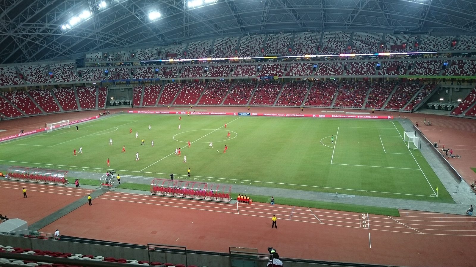 Vue générale d'un match de football de nuit au National Stadium de Singapour, avec les tribunes garnies et le toit éclairé