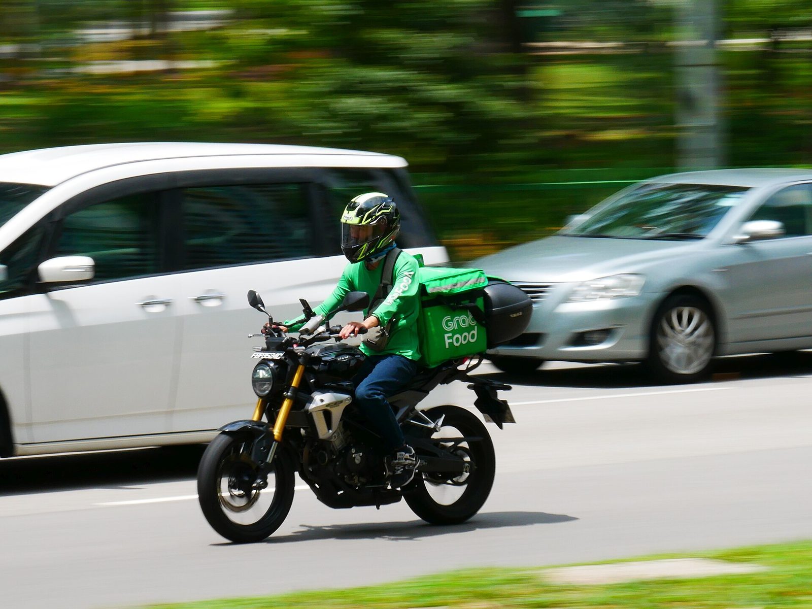 Un livreur casqué, en tenue verte, roule à moto avec un sac isotherme GrabFood dans une rue de Singapour