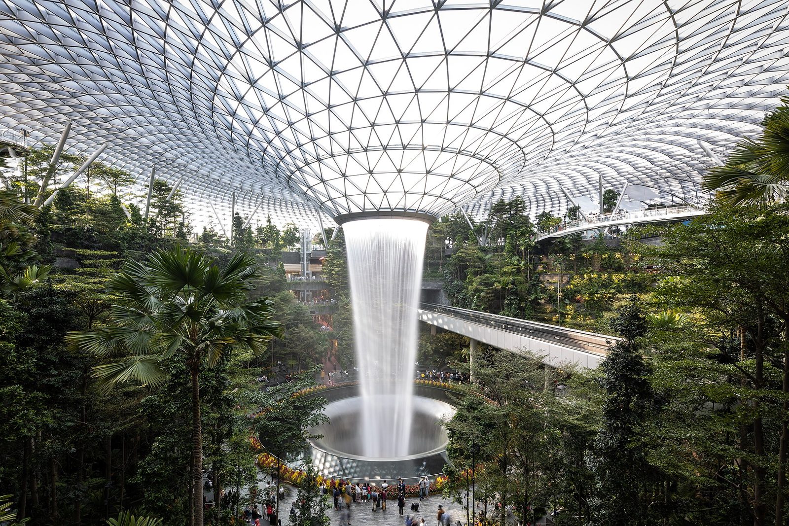 La cascade intérieure du Jewel à l'aéroport de Changi tombant sous une verrière, entourée d'une forêt tropicale et traversée par le Skytrain