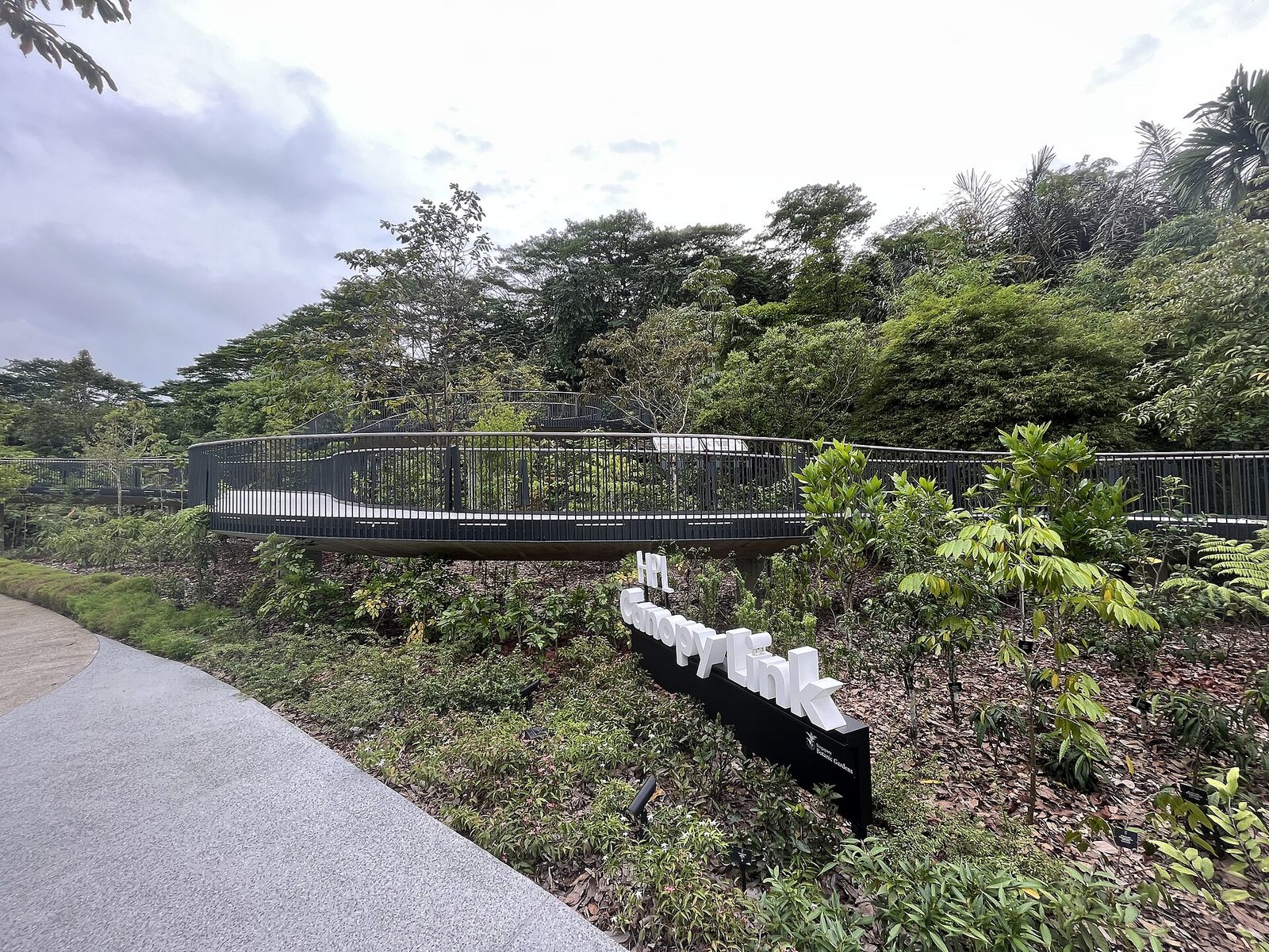 La passerelle HPL Canopy Link, bordée de garde-corps noirs, qui traverse la végétation du jardin botanique