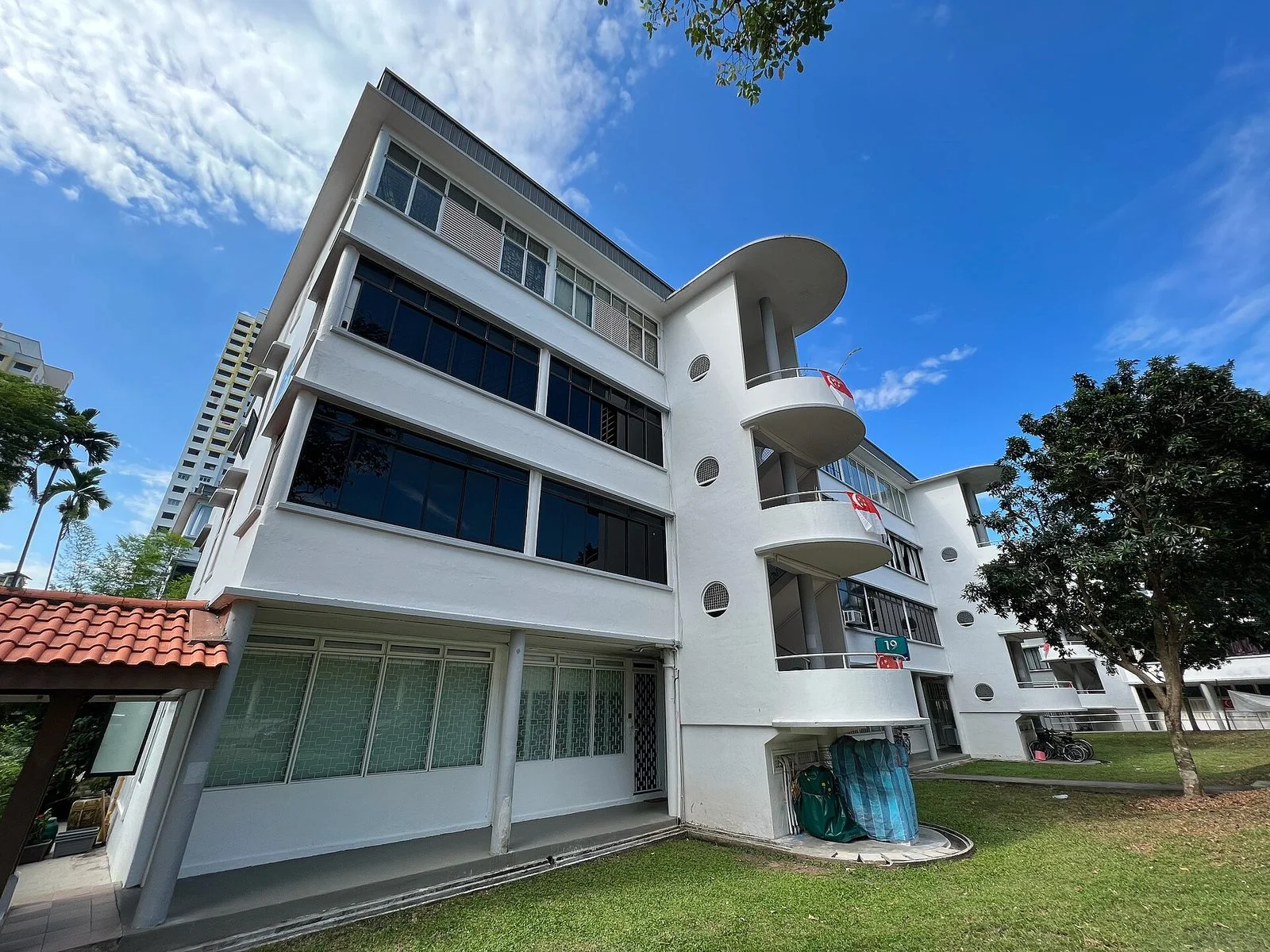 Immeuble d'habitation blanc aux balcons arrondis et hublots, entouré de pelouse et d'arbres, dans le quartier de Tiong Bahru