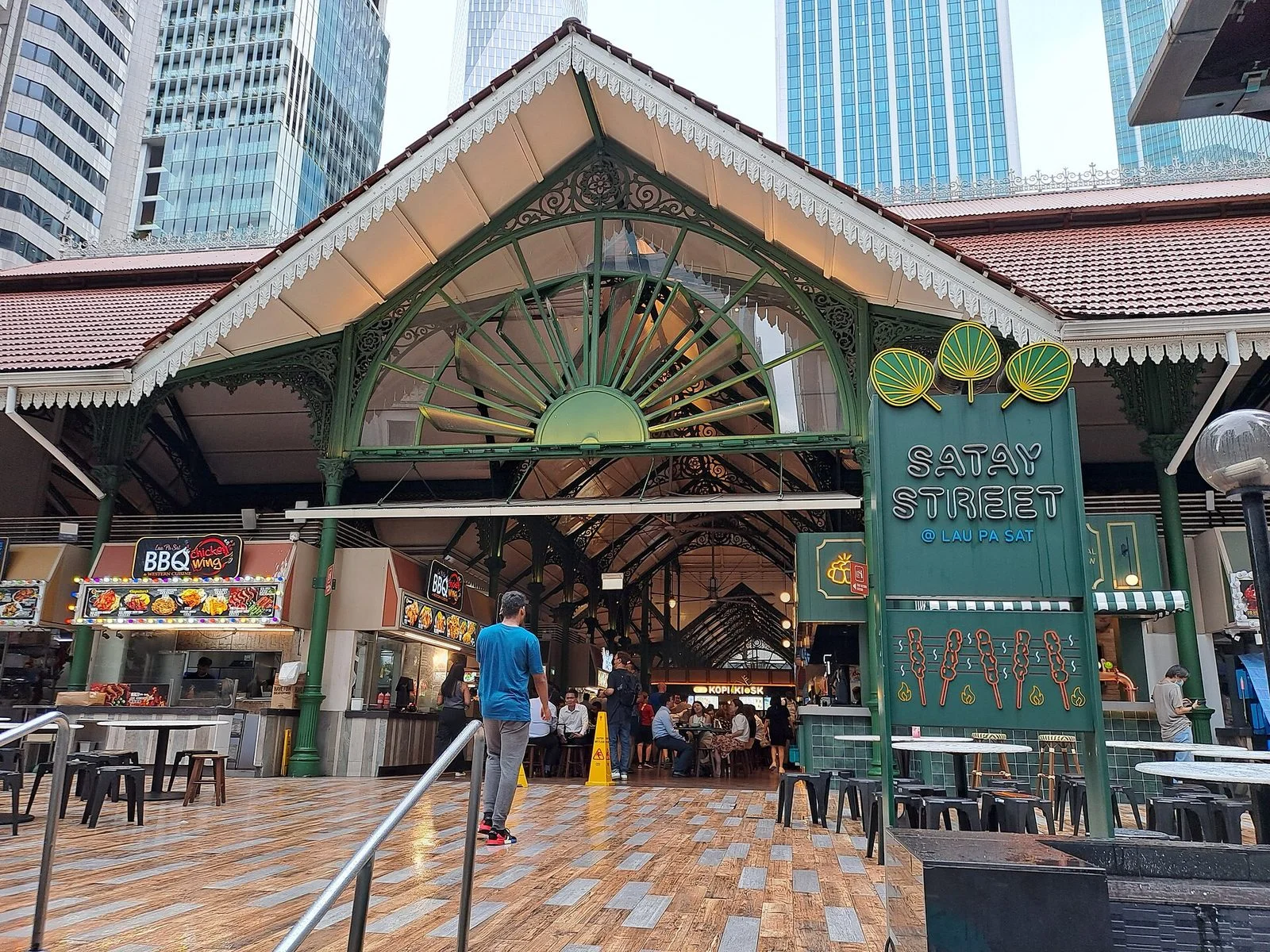 Entrée de la halle victorienne de Lau Pa Sat, avec son pignon en fonte verte et l'enseigne Satay Street, devant les tours du quartier d'affaires