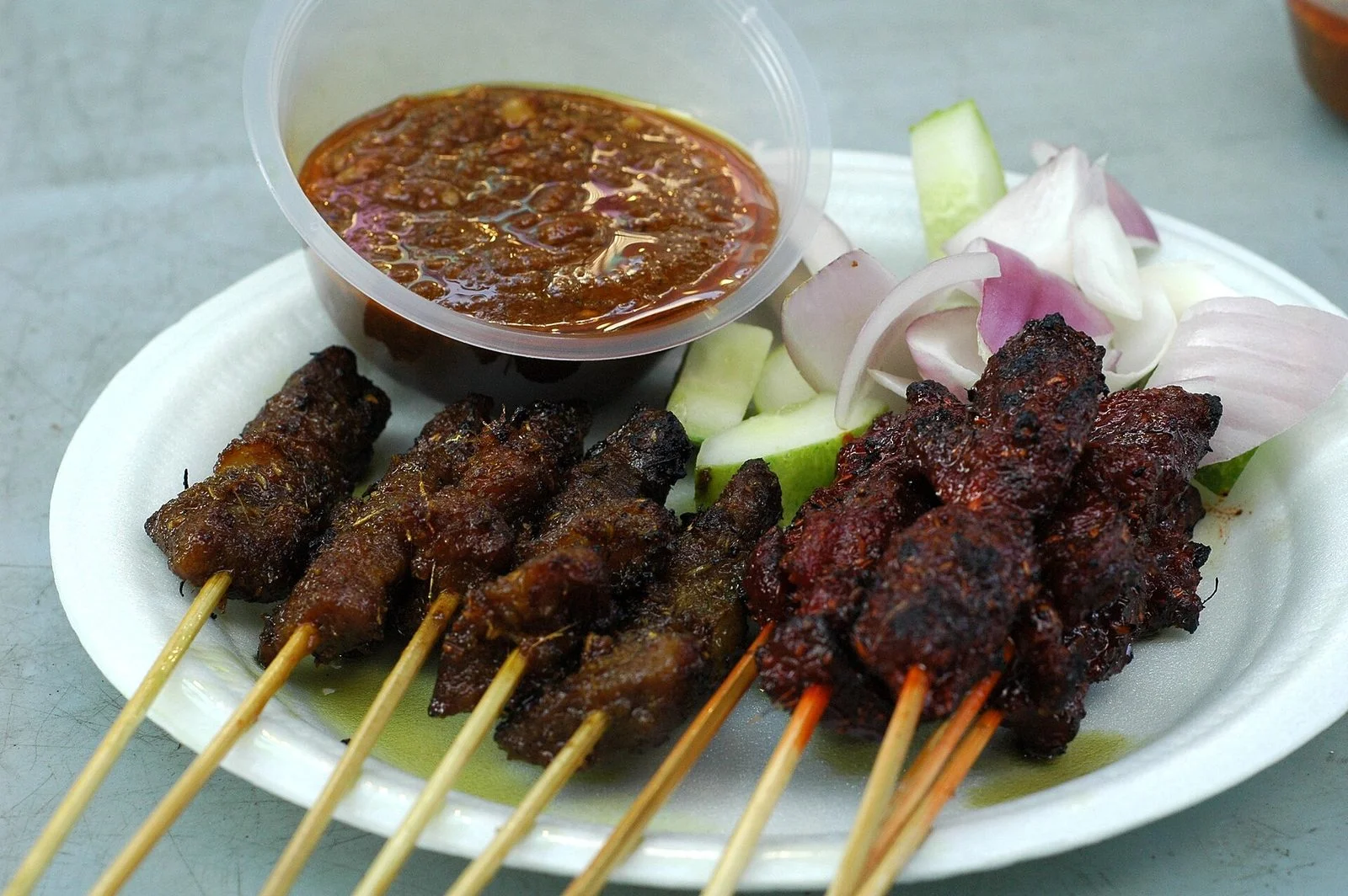 Assiette de brochettes de satay grillées avec un pot de sauce aux cacahuètes, des morceaux de concombre et d'oignon rouge