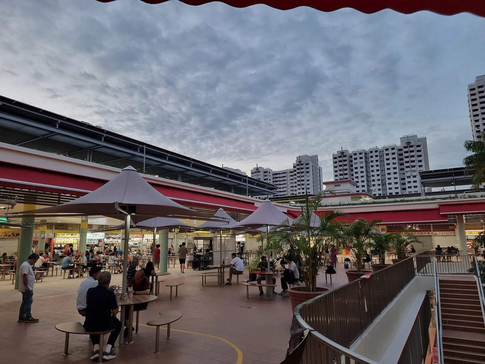 Terrasse en plein air du Tiong Bahru Market, avec des tables sous des parasols et des palmiers en pot, face aux stands