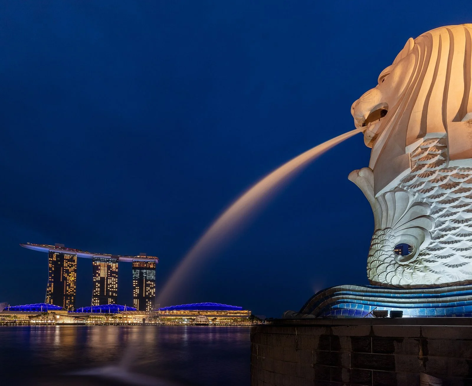Le Merlion illuminé crachant son jet d'eau dans Marina Bay, de nuit, avec les trois tours de Marina Bay Sands en arrière-plan